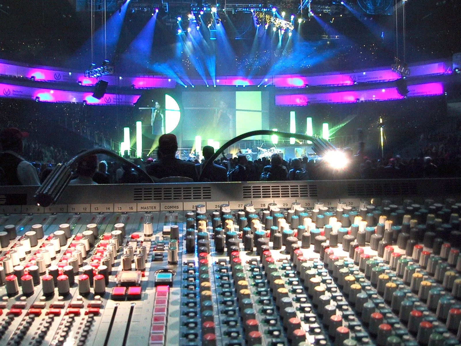 Großes FOH-Mischpult vor einer Arena-Bühne mit Lichtshow
