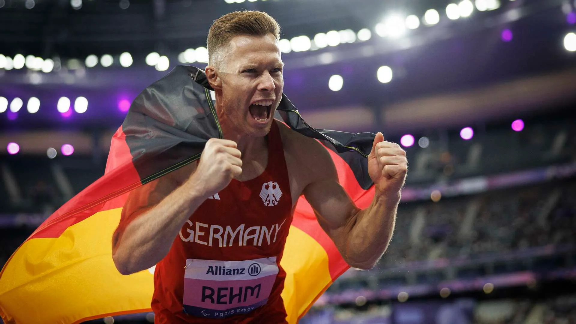 Markus Rehm jubelt mit der Deutschlandfahne im Stadion beim Para-Leichtathletik Heimspiel